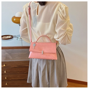 Detail of pink faux leather crossbody bag with silver buckle and key charm on model