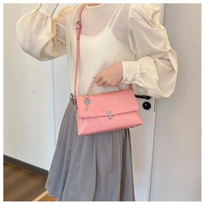 Detail view of pink leather handbag with silver turn-lock and key charm on model shoulder
