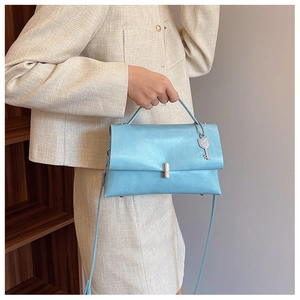 Detail of light blue faux leather bag with silver lock and key charm on beige outfit