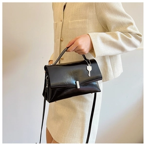 Detail of black glossy shoulder bag featuring silver hardware and a key-shaped metal charm