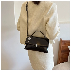 Detail of black glossy leather bag with metallic silver key charm and adjustable strap
