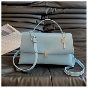 Detail of light blue crossbody bag with silver lock and key charm on black sofa