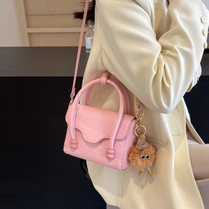 Pink croc-embossed mini crossbody bag with plush bear charm on light blazer backdrop