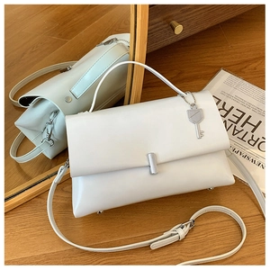 Detail of white leather shoulder bag with silver buckle and unique key charm on wood floor