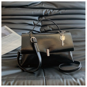 Detail of glossy black leather bag with silver key charm and metallic cylinder lock