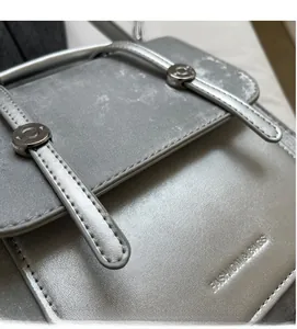 Close-up of textured silver leather bag showing metallic buckles and fashion logo