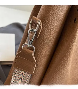 Macro shot of silver metal clip and colorful geometric woven strap on brown leather bag