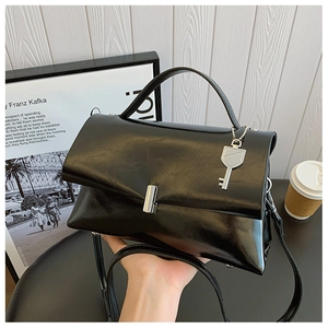 Detail of black glossy leather bag with silver buckle and decorative key pendant