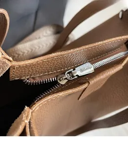 Detailed close-up of smooth silver metal zipper and brown litchi grain leather texture