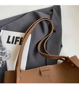 Detail of reinforced double shoulder straps and lychee texture on brown leather tote