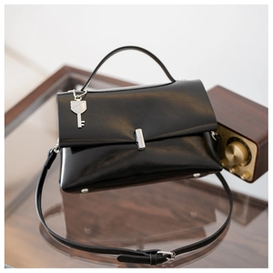 Detail of black leather crossbody bag with silver key charm on a glass table