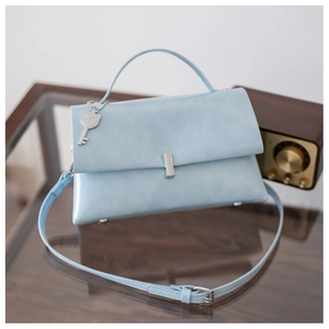 Close-up of light blue oil wax leather crossbody bag with vintage key charm on glass table