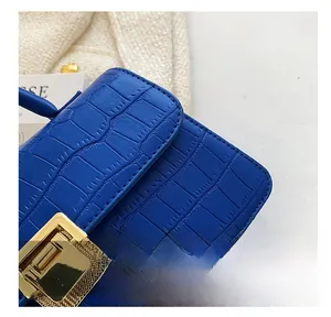 Detail of blue crocodile pattern handbag showing golden metal lock and precision stitching