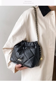 Detail of black quilted chain bag with gold sphere charm on a beige coat outfit