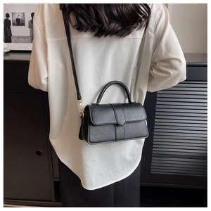 Rear view of a minimalist black leather handbag worn as a crossbody bag in a modern setting