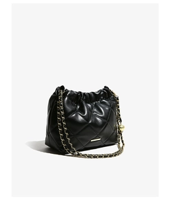 Detail of black quilted bucket bag featuring a gold chain strap and decorative metal ball