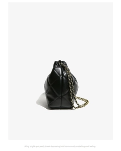 Close-up of quilted black patent leather bucket bag with golden chain strap detail