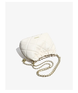 Detail of white quilted drawstring bucket bag with gold chain strap and metal ball