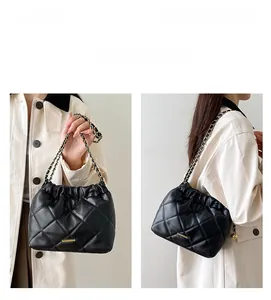 Detailed view of black quilted bucket bag with chain strap shown on beige trench coat