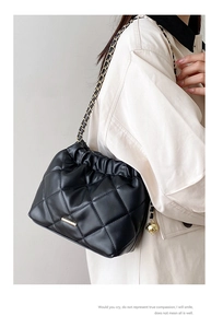 Detail of black quilted leather bucket bag with gold chain and drawstring closure