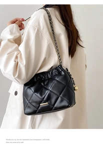 Detail of black quilted leather bucket bag with gold chain strap and drawstring closure