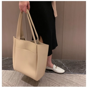 Gros plan d'un cabas en cuir beige avec poche frontale pratique tenu par un mannequin en studio