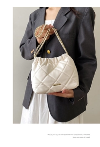 Detail view of cream quilted bucket bag with gold chain strap and elegant metal trim