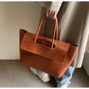 Detailed view of caramel brown tote bag with crocodile texture carried by a model