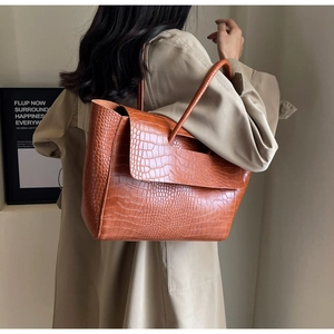 Detail of a large brown croc-embossed tote bag worn with a classic beige trench coat