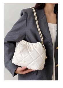 Detail of quilted beige bucket bag with chain strap and soft cloud-like pleated top closure