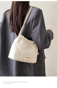 Detail of beige quilted bucket bag with gold chain strap worn over a grey blazer