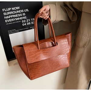 Detail of a brown crocodile texture tote bag shown in a professional lifestyle setting