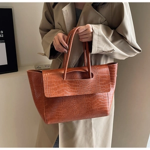 Detail of caramel crocodile pattern leather tote bag carried by model in a trench coat