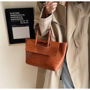 Detail of a brown crocodile-embossed tote bag with handle and flap closure style