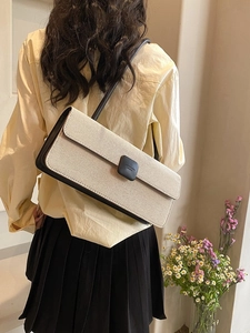 Detail of minimalist cream canvas baguette bag with black leather trim and shoulder strap