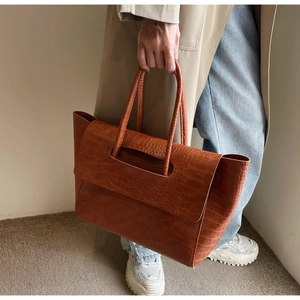 Detail of large orange-brown tote bag with faux crocodile texture and hollow handle