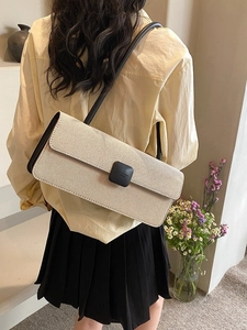 Detail of cream canvas baguette bag with black trim worn on shoulder by a model