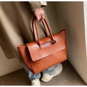 Brown crocodile embossed tote bag with large capacity held by a hand in a minimalist setting