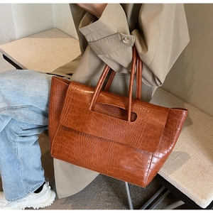Detail view of brown crocodile embossed tote bag with vintage texture on a model's arm