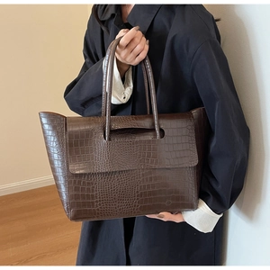 Close-up of brown crocodile texture on a large tote bag with top handles and flap detail