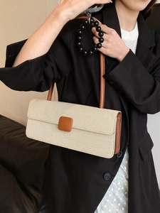 Detailed view of cream canvas baguette bag with brown leather trim worn under the arm