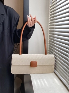 Detail of cream woven baguette bag with brown leather strap held by a model