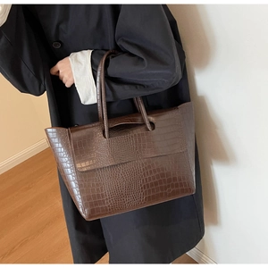Side view of large dark brown crocodile pattern tote bag held by model in black coat