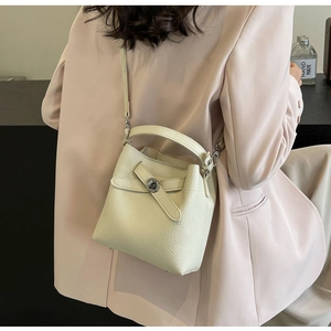 Detail der cremefarbenen Eimer-Tasche mit Lychee-Ledertextur und Metall-Drehverschluss