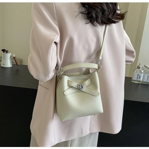 Cremeweiße Eimertasche mit Lychee-Struktur und silbernem Drehverschluss am Modell