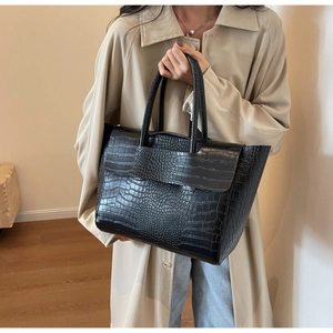 Detail of black tote bag with faux crocodile texture held by model in beige trench coat