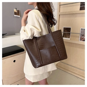 Detail view of dark brown tote bag with crocodile texture on a model in beige blazer
