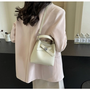 Detail einer beigen Eimer-Tasche aus genarbtem Leder mit silberner Schnalle und Schultergurt