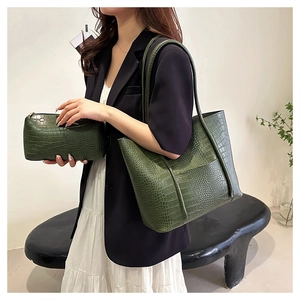 Close-up of green crocodile embossed tote bag and clutch set on a stylish model