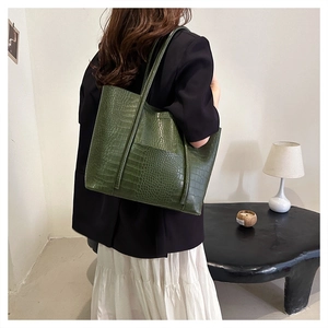 Detailed view of deep green tote bag with crocodile pattern texture on model shoulder